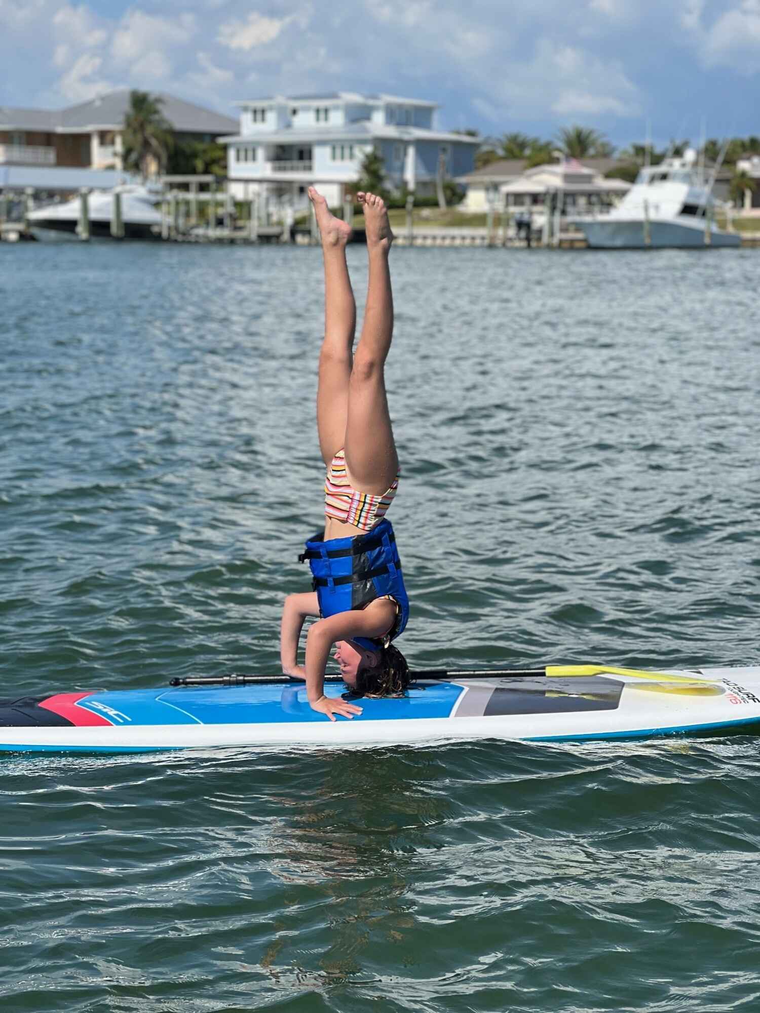 Young girl doing a headstand on a paddle board in the ocean